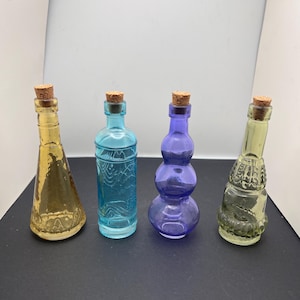 Puede incluir: Cuatro botellas decorativas de vidrio con tapones de corcho. Las botellas son en tonos amarillo, azul y morado. Las botellas tienen diferentes formas y texturas. Perfectas para la decoración del hogar o manualidades.