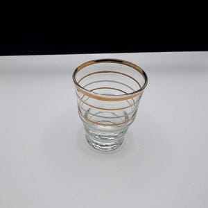 Könnte beinhalten: Ein klares Glas-Schnapsglas mit goldenen Streifen um den Rand und den Körper.