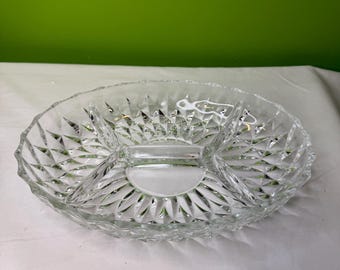 Op de afbeelding: Een heldere, ovale glazen serveerschaal met vier compartimenten. De schaal heeft een diamantgeslepen patroon langs de randen en op de verdelers. Het middengedeelte is rond. Ontworpen voor het serveren van snacks of hapjes.