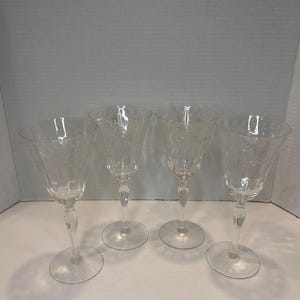 May include: Set of four clear glass wine glasses with a cut glass design. The glasses have a tall, slender stem and a round bowl.