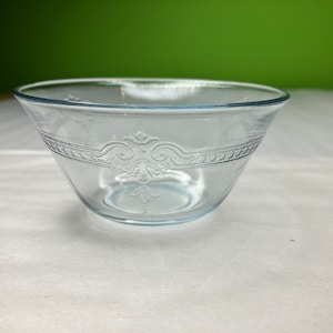 Peut inclure: Un bol en verre transparent avec un motif gravé délicat autour du bord. Le bol est de couleur bleu clair et a une forme arrondie.