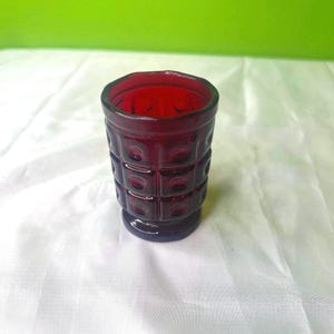 Op de afbeelding: Een diep rood glazen shotglas met een getextureerd, vierkant patroon. Het glas heeft een afgeronde bodem.