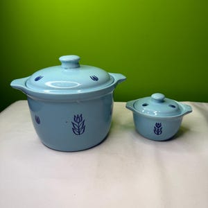 Op de afbeelding: Twee lichtblauwe keramische potten met deksels. De grotere pot heeft een inhoud van ongeveer 1,4 liter, en de kleinere pot heeft een inhoud van ongeveer 240 ml. Beide potten hebben donkerblauwe bloemmotieven.