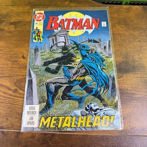 May include: A white ceramic mug with a black handle and the text "But First, Coffee" in a black, bold font. The mug is sitting on a wooden surface. The mug is approximately 4 inches tall.