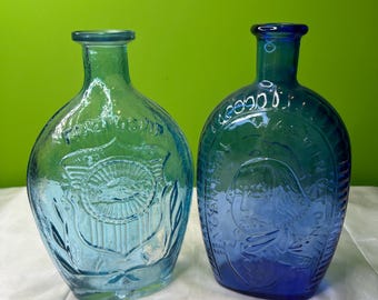 Peut inclure: Deux flacons en verre avec des cols étroits et des corps arrondis. Le flacon bleu clair présente un motif de bouclier en relief avec le mot FRIENDSHIP. Le flacon bleu foncé affiche un portrait en relief de George Washington avec le texte WASHINGTON.