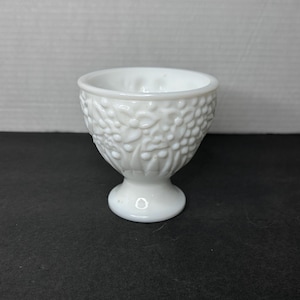 以下が含まれることがあります： 花柄の白いミルクガラスの卵カップ。カップは台座付きです。