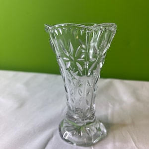 May include: A clear glass vase with a diamond pattern. The vase has a flared top and a wide base.
