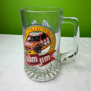 Puede incluir: Taza de cerveza de vidrio transparente con asa, con un gráfico colorido de un coche de carreras con el número 44, las palabras "1995 Collectors Edition" y el logotipo de Slim Jim Racing Team. La taza tiene una base decorativa.
