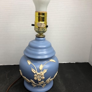 May include: A blue ceramic table lamp with a white floral design. The lamp has a white light bulb and a gold-colored switch.