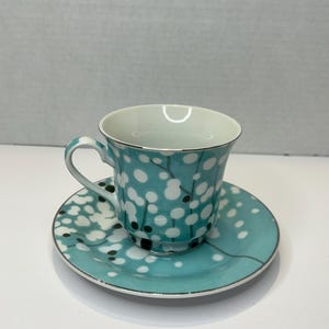 May include: A teal blue teacup and saucer set with a white and black floral pattern.