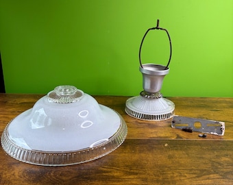La pantalla de lámpara de techo Art Déco vintage presenta un distintivo centro de vidrio transparente con un patrón acanalado que irradia desde el centro y un cuerpo en forma de cúpula blanca esmerilada.