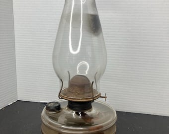 May include: A vintage glass kerosene lamp with a clear glass chimney and a metal base. The lamp has a round, clear glass reservoir and a metal wick adjuster.