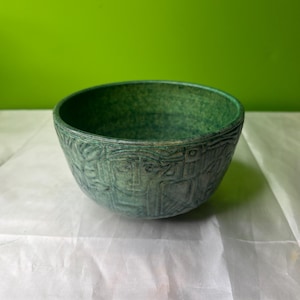 May include: A green ceramic bowl with a textured, embossed design. The bowl is round and has a wide rim.