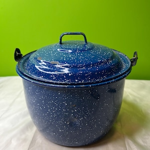 Könnte beinhalten: Ein blauer Emaille-Topf mit passendem Deckel und weißen Sprenkeln. Der Topf hat einen Griff am Deckel und zwei seitliche Griffe. Der Topf ist dunkelblau. Er wird wahrscheinlich zum Kochen verwendet.