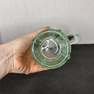 May include: A clear glass mug with a green tint and a handle. The mug has a textured, ribbed design.