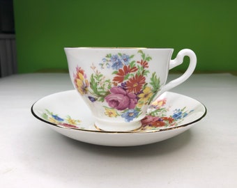 May include: A white teacup and saucer with a floral pattern. The cup and saucer have a gold trim around the edges. The floral pattern features pink, red, yellow, and blue flowers.