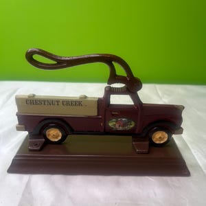 Peut inclure: Un casse-noix en métal marron en forme de camionnette vintage. La benne du camion est beige avec les mots "CHESTNUT CREEK". Les roues sont dorées et le levier du casse-noix est marron. Une petite image ovale d'une grange est sur la porte du camion.