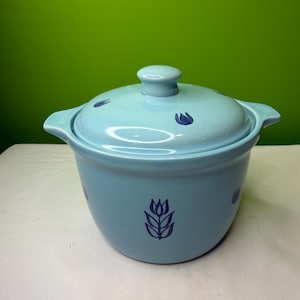 Op de afbeelding: Een lichtblauwe keramische ovenschaal met een deksel. De schaal heeft twee handvatten en is versierd met donkerblauwe tulpenontwerpen. Het deksel heeft een kleine knop en bijpassende tulpenaccenten. De schaal staat op een wit oppervlak.