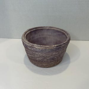 May include: A purple ceramic planter with a rope-like texture. The planter is round and has a wide opening.