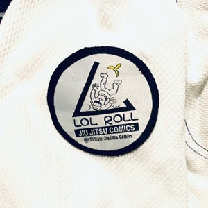May include: White Jiu-Jitsu Gi with a black and white patch that says "LOL ROLL JIU JITSU COMICS" and features a cartoon of a person being thrown. The patch also includes the social media handle "@LOL_Roll_Jiu_Jitsu_Comics".