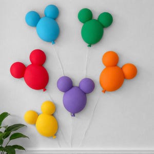 Könnte beinhalten: Eine Anordnung aus sechs mausförmigen Ballon-Sets, die jeweils aus einem großen zentralen Ballon mit zwei kleineren, oben angebrachten runden Ballons bestehen. Die Ballons sind in Blau, Grün, Rot, Orange, Lila und Gelb gehalten.
