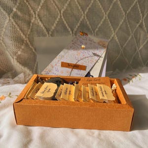 May include: An orange rectangular box filled with small, labeled cards. The cards are arranged neatly inside the box. A recipe card with the word "recipes" is visible in the background.
