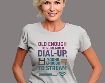 以下が含まれることがあります： OLD ENOUGH TO REMEMBER DIAL-UP, YOUNG ENOUGH TO STREAMというテキストがプリントされたライトグレーの半袖Tシャツ。デザインには、フロッピーディスク、モデム、読み込みバー、Wi-Fiアイコンのグラフィックが青と紫の色合いで描かれています。