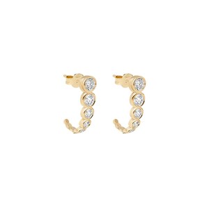 May include: A pair of gold hoop earrings featuring a curved design with five bezel-set round clear stones of graduating sizes along the front edge, finished with a post back closure for secure attachment to the earlobe.