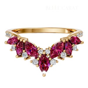 Może przedstawiać: Złoty pierścionek o unikalnym wzorze. Pierścionek posiada szereg markizowych, ciemnoróżowych kamieni szlachetnych, zaakcentowanych małymi, okrągłymi, przezroczystymi kamieniami szlachetnymi. Obręcz pierścionka jest również złota, a w tle widoczny jest napis "BELLE CARAT".