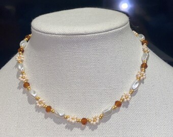 May include: A delicate gold necklace with white oval beads and brown glass beads.