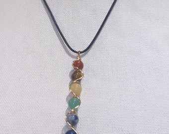 May include: A black cord necklace with a gold wire wrapped pendant featuring seven colorful gemstone beads.