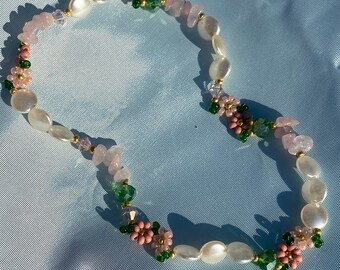 May include: A delicate necklace made with white and pink beads, green and gold accents, and small pink flower charms.