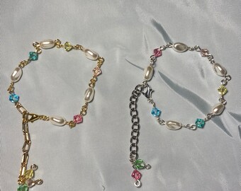 May include: Two delicate bracelets with pearl and crystal accents. One bracelet is gold with a charm, the other is silver.