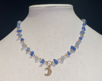 Könnte beinhalten: Eine zarte goldene Kettenkette mit einem Halbmond-Anhänger. Die Kette ist aus hellblauen und dunkelblauen Edelsteinperlen gefertigt.