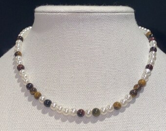 May include: A white pearl and tiger's eye beaded necklace. The necklace is made with alternating white pearls and brown, gold, and red tiger's eye beads.
