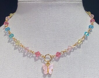 May include: A gold chain necklace with a pink butterfly charm. The chain is decorated with small, colorful beads in shades of blue, green, pink, and yellow.