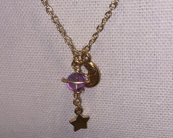 May include: A gold chain necklace with a purple glass orb pendant, a crescent moon charm, and a star charm.