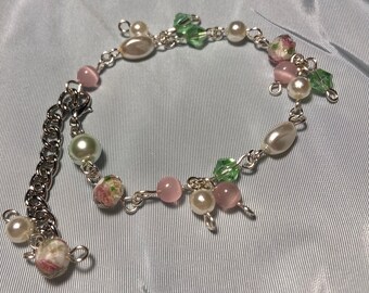 May include: A delicate silver chain bracelet with pink and white pearl beads, green glass beads, and floral accents.