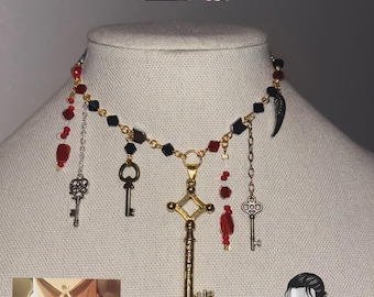 May include: A gold-toned necklace with multiple key pendants and red and black bead accents. The necklace features a large, ornate key pendant and smaller key charms. The design is inspired by the anime series Attack on Titan.