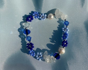 Könnte beinhalten: Ein blaues und weißes Perlenarmband mit blütenförmigen Anhängern und weißen Perlenakzenten. Das Armband ist aus kleinen Glasperlen gefertigt und hat einen zarten, femininen Look.