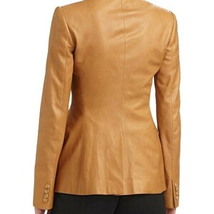 May include: A tan leather blazer with a notched collar and long sleeves. The blazer has a single-breasted closure and two front pockets.