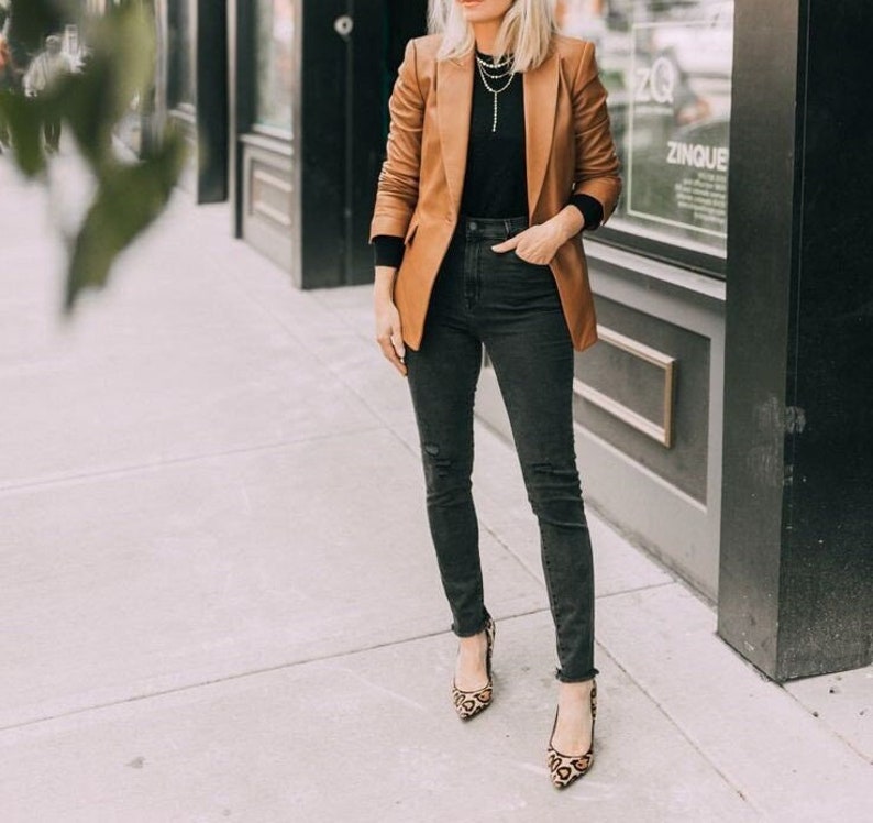 May include: A woman wearing a brown blazer, black turtleneck, black jeans, and leopard print heels.