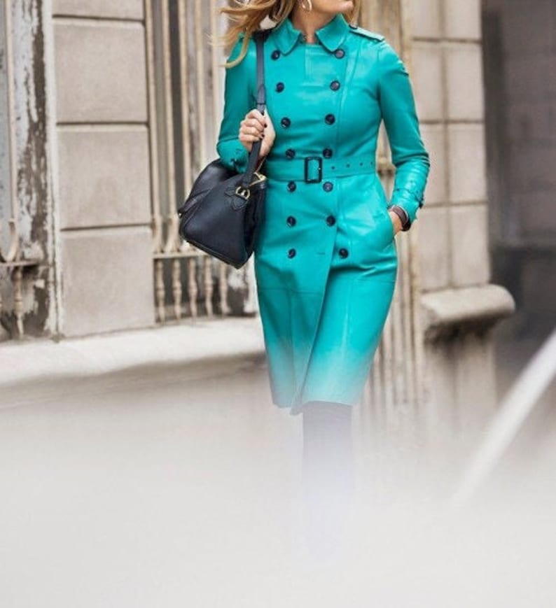 May include: A turquoise leather trench coat with a double breasted closure, a belt, and a black bag.