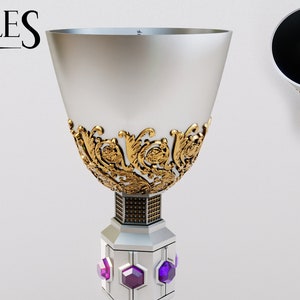 以下が含まれることがあります： 紫色の宝石のアクセントが付いた、装飾的なディテールが施された銀と金の聖杯。聖杯は、幅広の溝付きボウルと詳細なベースを備えています。画像には「PUZZLES AND PROPS」というテキストとロゴが含まれています。