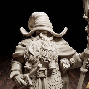 May include: A white painted miniature figurine of a dwarf wizard holding a staff with a three-pronged top. The dwarf is wearing a pointed hat, a long beard, and a chainmail tunic. The figurine is standing on a black base and next to a yellow 20-sided die.