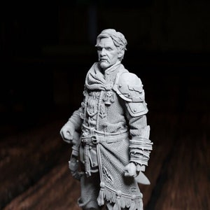 May include: A detailed grey figurine of a man in medieval clothing, standing on a black circular base. The figure is holding a small knife. A yellow, twenty-sided die rests nearby on a wooden surface.