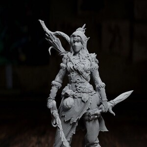 May include: A grey 3D printed miniature of a female elf warrior with a bow and arrow, wearing a leather outfit and a mask. The miniature is standing on a black base and next to a yellow 20-sided die.