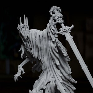 May include: A grey, skeletal figure wearing a tattered robe and holding a sword stands on a base with a broken tombstone. The figure is surrounded by a swirling mist.