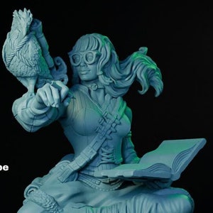 Puede incluir: Una miniatura impresa en 3D de una figura femenina con cabello castaño corto, que lleva gafas y una túnica marrón, sosteniendo un libro y un gallo. La figura está sentada en un barril de madera con una cuerda envuelta alrededor. La miniatura está pintada de azul claro. El texto "Helen Journey Scribe" es visible debajo de la figura.