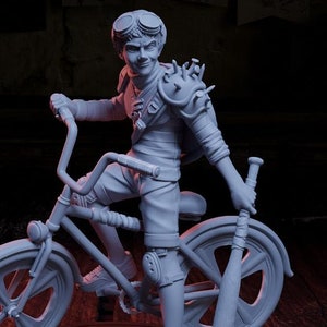 May include: A white painted miniature figurine of a young person riding a bicycle with a baseball bat in their hand. The figurine is on a black circular base. A yellow 20-sided die is in the foreground.